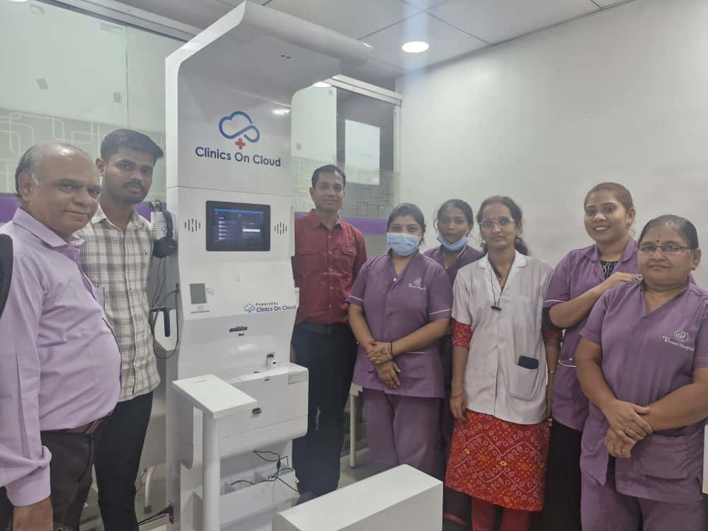 Group of hospital staff and visitors posing beside a Clinics On Cloud health kiosk indoors.