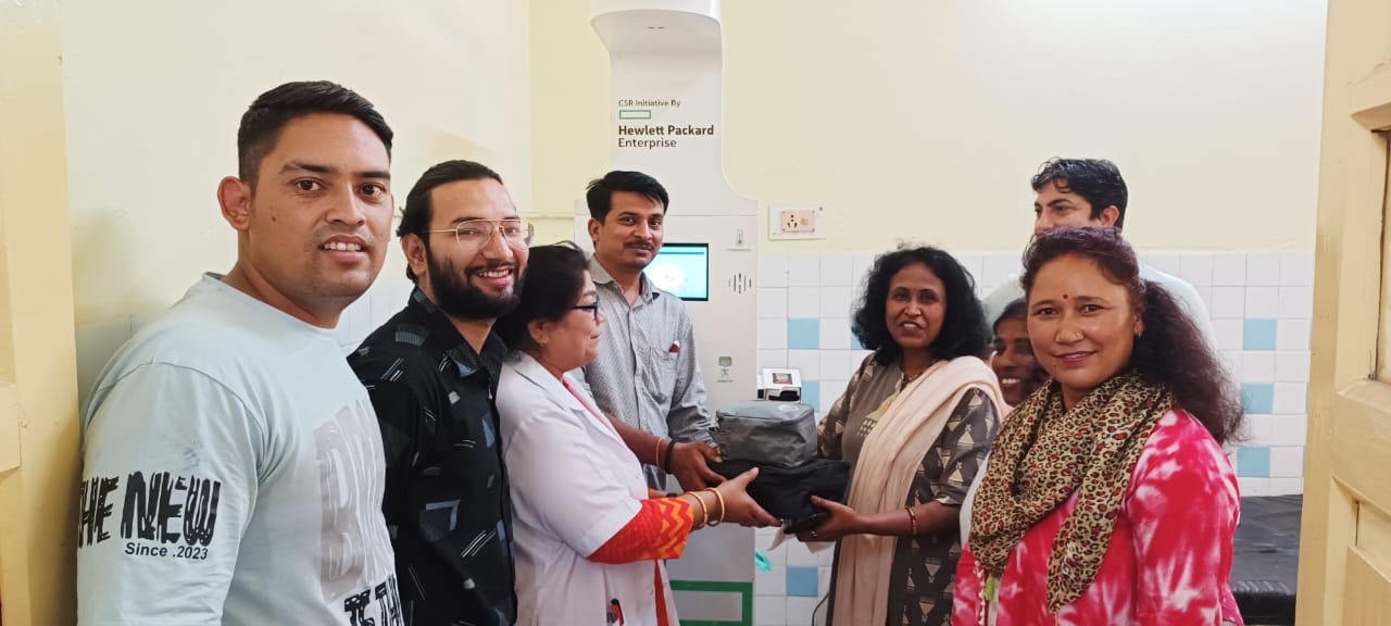 Group poses beside a health kiosk with Hewlett Packard Enterprise CSR branding, handing over an equipment case.